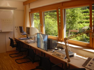 Ein heller, mit Computern und technischen Geräten ausgestatteter Raum mit großen Fenstern, die eine grüne Landschaft zeigen.