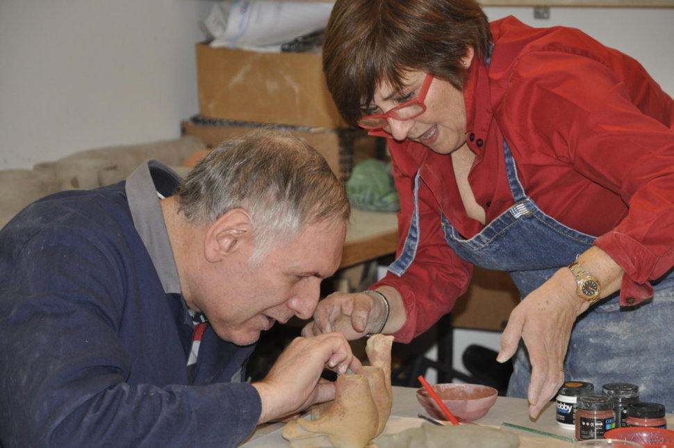 Eine Frau unterstützt einen Mann beim Töpfern, beide konzentrieren sich auf das Detail der Tonarbeit.
