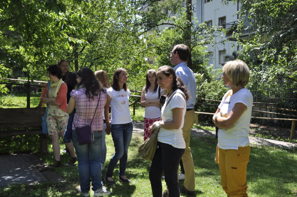 Un gruppo di persone è riunito in un giardino verdeggiante in una giornata soleggiata e chiacchiera.