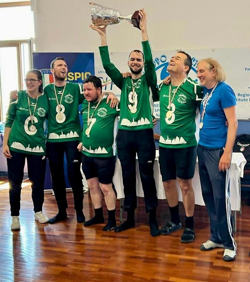 Eine Gruppe von sechs Menschen in grünen Trikots steht zusammen, eine Person hält einen Pokal in die Luft.
