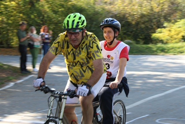 Ein Mann und eine Frau fahren gemeinsam auf einem Tandemfahrrad, beide mit Helmen, während sie sich auf einem sonnigen Weg befinden.